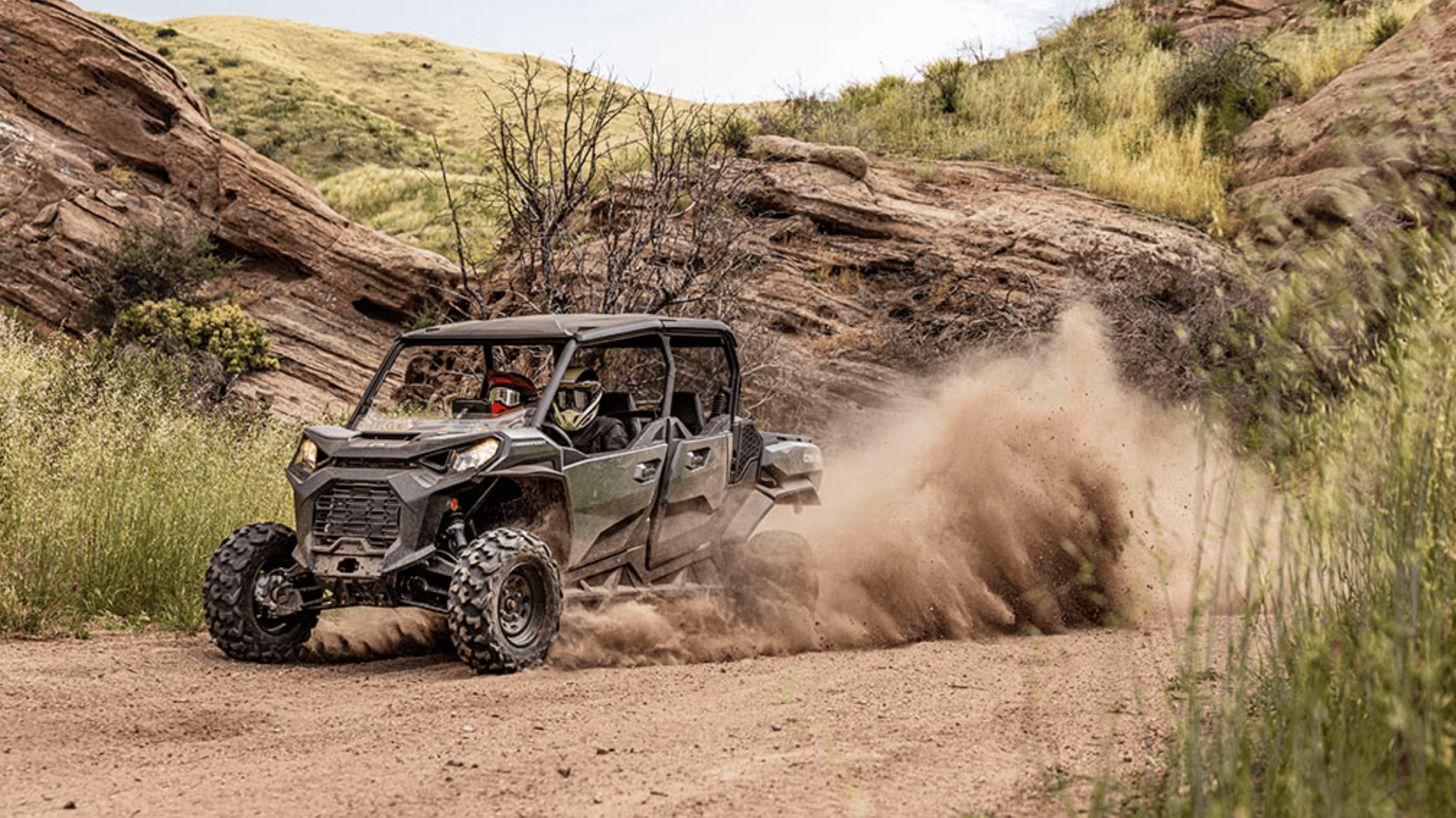 Off-road 2025 Can-Am Commander kicks up dust while driving through rugged terrain.