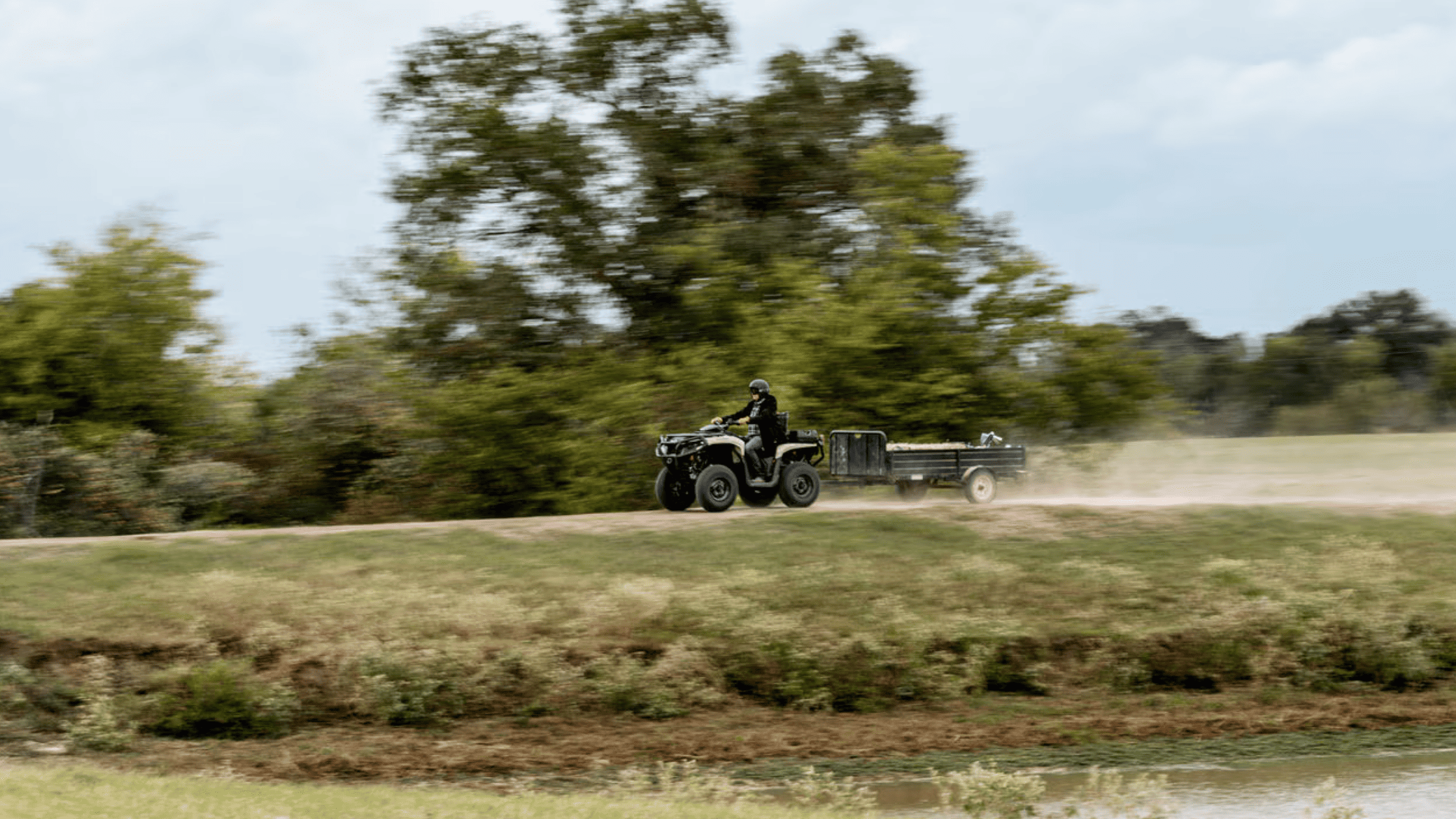 2025 Can-Am Outlander PRO ATV towing a trailer across a grassy field.