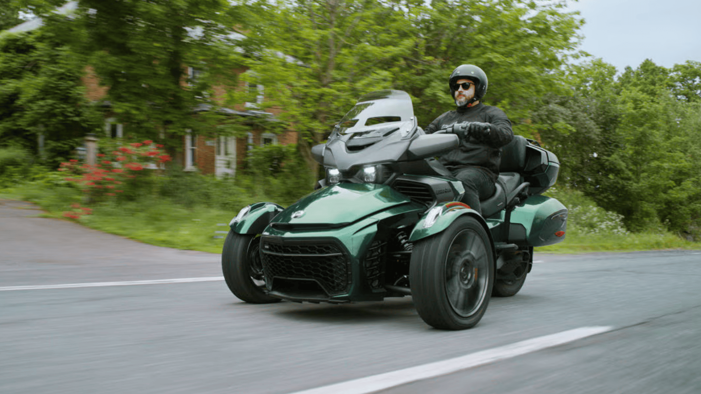 2025 Can-Am Spyder F3 in green being ridden on a rural road with trees and houses in the background