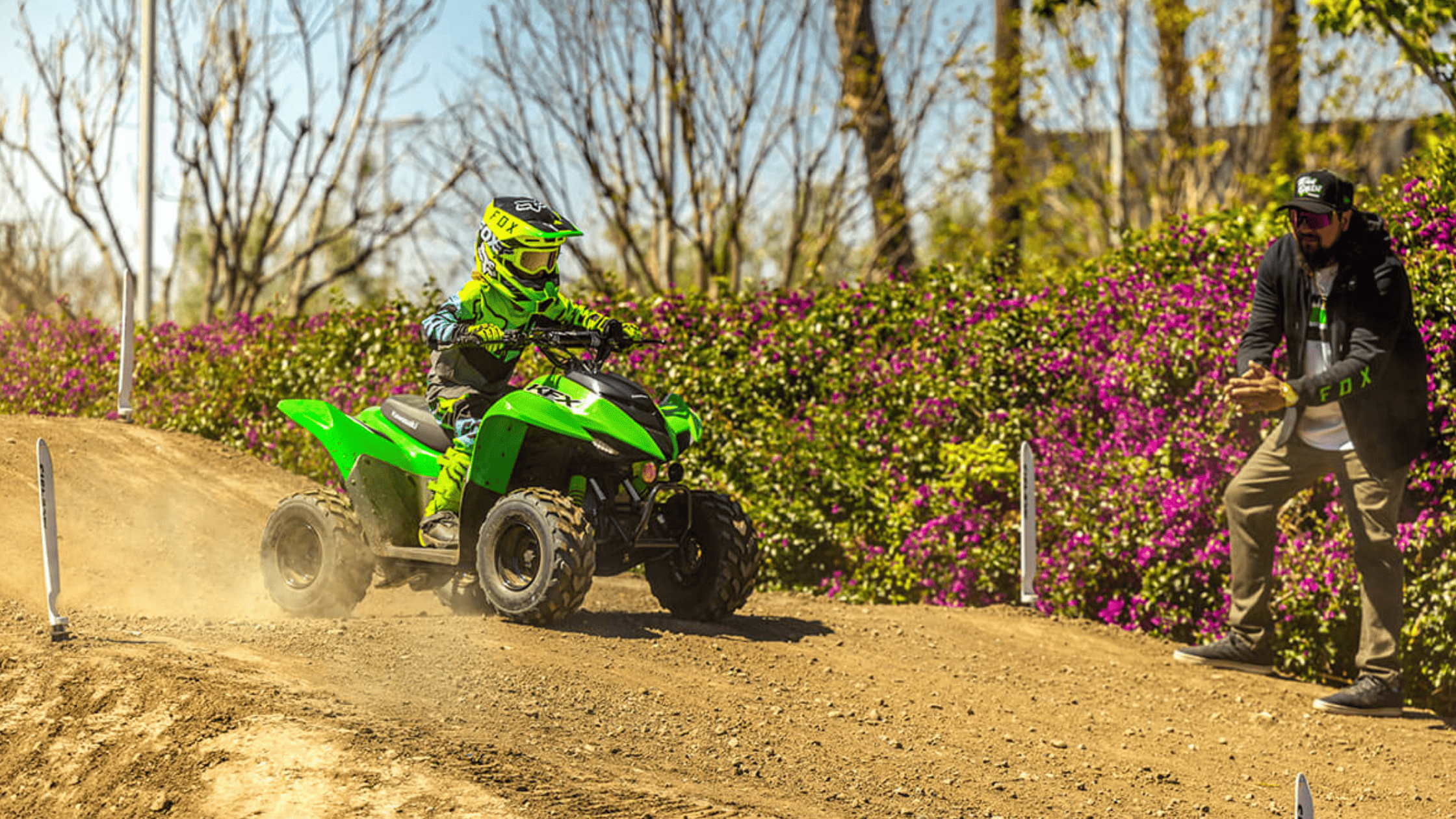 Child riding a 2025 Kawasaki KFX®50 ATV on a dirt trail with adult guidance.