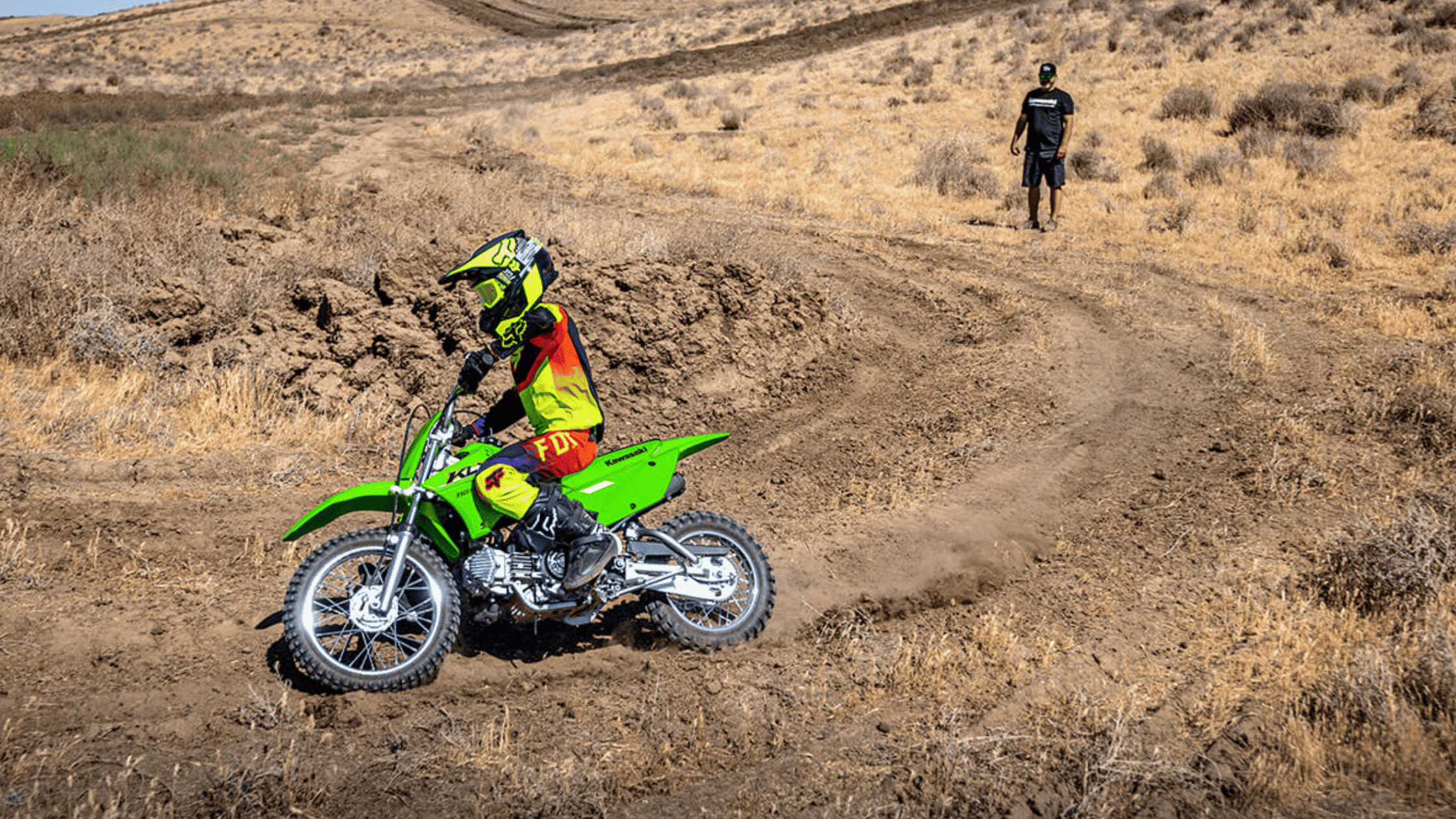 Young rider on 2025 Kawasaki KLX 110R dirt bike riding on a dry off-road trail.