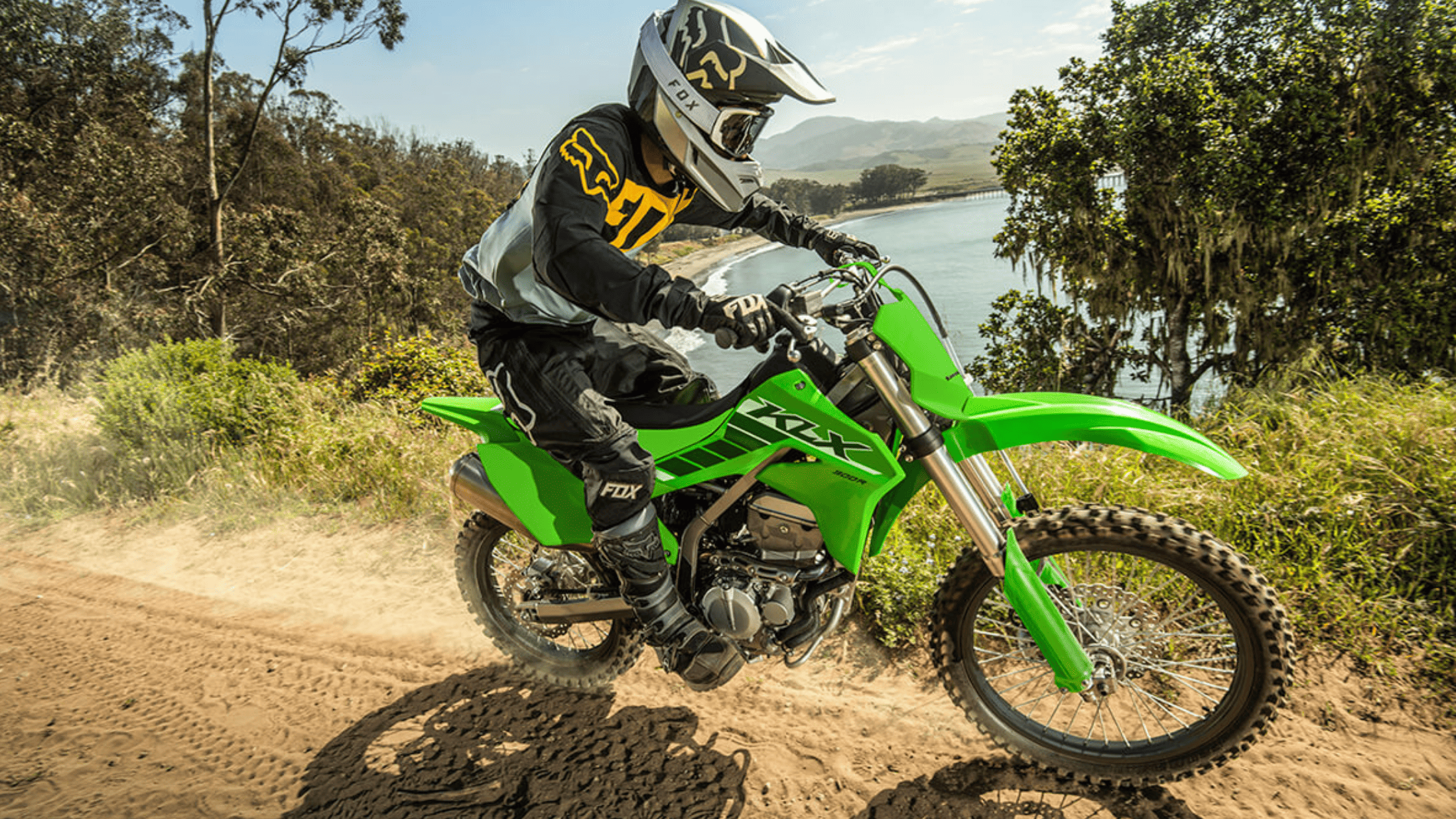 Rider on a green Kawasaki KLX®300R dirt bike navigating a coastal trail.